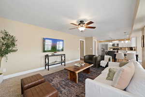 Living room with carpet, baseboards, and ceiling fan with notable chandelier