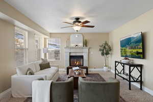 Carpeted living room with ceiling fan, baseboards, a textured ceiling, and a glass covered fireplace