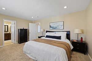 Bedroom with a textured ceiling, recessed lighting, light colored carpet, baseboards, and ensuite bath