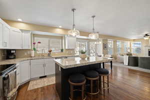 Kitchen featuring dark wood-type flooring, open floor plan, a kitchen island, a sink, and stainless steel electric range