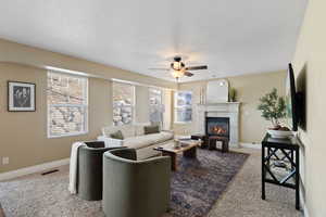 Carpeted living room with visible vents, baseboards, a ceiling fan, a glass covered fireplace, and a textured ceiling