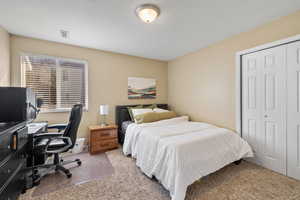 Carpeted bedroom with a textured ceiling, a closet, and visible vents