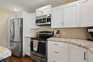 Kitchen with light stone counters, dark wood finished floors, stainless steel appliances, recessed lighting, and white cabinets