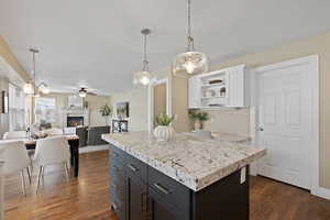 Kitchen with a lit fireplace, white cabinetry, open shelves, and dark wood-style flooring