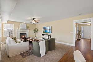 Living area featuring wood finished floors, a glass covered fireplace, a ceiling fan, and baseboards