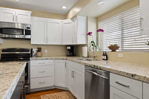 Kitchen with recessed lighting, stainless steel appliances, a sink, white cabinets, and dark wood finished floors