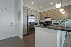 Kitchen with range hood, stainless steel appliances, dark countertops, a sink, and a peninsula