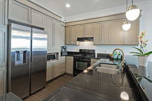 Kitchen featuring under cabinet range hood, dark tile patterned floors, a sink, appliances with stainless steel finishes, and decorative light fixtures