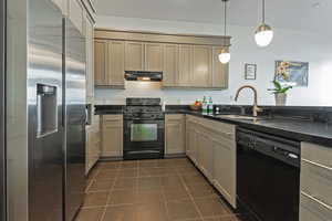 Kitchen featuring dark countertops, under cabinet range hood, black appliances, dark tile patterned floors, and a sink