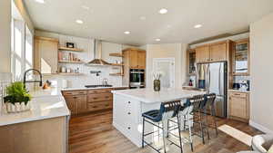 Kitchen featuring a breakfast bar, open shelves, appliances with stainless steel finishes, a kitchen island, and wall chimney range hood