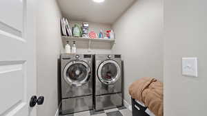 Clothes washing area with laundry area, washing machine and dryer, baseboards, and tile patterned floors