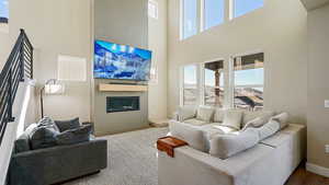 Living area featuring visible vents, baseboards, a glass covered fireplace, a towering ceiling, and dark wood-style flooring