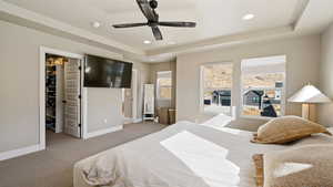 Carpeted bedroom with a spacious closet, baseboards, a tray ceiling, and recessed lighting