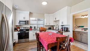 Kitchen featuring stainless steel appliances, white cabinets, a sink, and wood finished floors