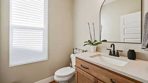 Half bath featuring baseboards, vanity, toilet, and a healthy amount of sunlight