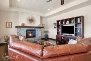 Living room with dark wood-style flooring, a raised ceiling, a stone fireplace, and baseboards