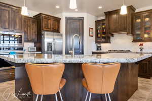 Kitchen with appliances with stainless steel finishes, a large island with sink, and glass insert cabinets