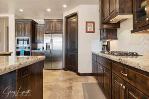 Kitchen featuring stainless steel appliances, light stone counters, and dark brown cabinets