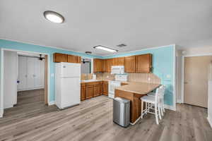 Kitchen with white appliances, visible vents, brown cabinetry, and light countertops