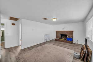 Unfurnished living room featuring a brick fireplace, visible vents, a textured ceiling, and wood finished floors