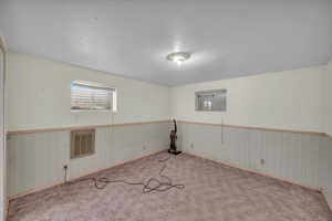 Carpeted empty room with a wainscoted wall, visible vents, and a textured ceiling