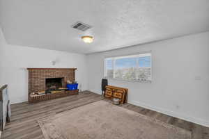 Living area featuring a textured ceiling, a brick fireplace, wood finished floors, and visible vents