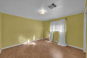 Unfurnished room with visible vents, crown molding, baseboards, and wood finished floors