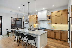 Kitchen featuring light wood-type flooring, premium range hood, a sink, and open shelves