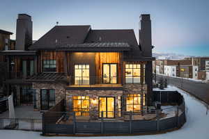 Back of property with a patio, a chimney, fence, a balcony, and stone siding