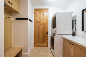 Laundry room with baseboards, stacked washer and clothes dryer, cabinet space, and stone tile floors