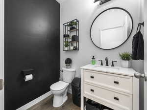 Half bathroom featuring toilet, baseboards, wood finished floors, and vanity