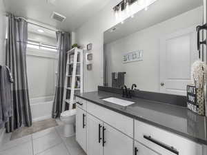 Bathroom featuring visible vents, shower / bathtub combination with curtain, toilet, vanity, and tile patterned flooring