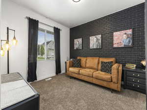 Living area featuring baseboards, visible vents, brick wall, an accent wall, and carpet flooring