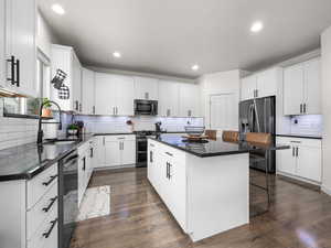 Kitchen with stainless steel appliances, dark countertops, a sink, a kitchen island, and a kitchen bar