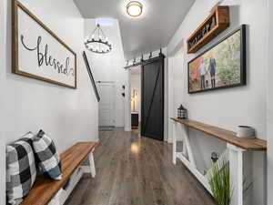 Hallway with dark wood-style floors, a barn door, baseboards, and an inviting chandelier