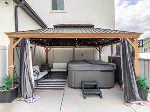 View of patio featuring visible vents, fence, a hot tub, and a gazebo