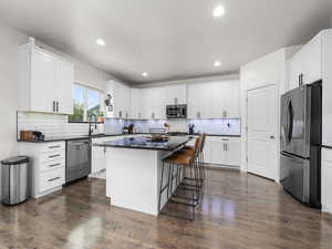 Kitchen featuring appliances with stainless steel finishes, dark countertops, dark wood-type flooring, and a kitchen island