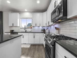 Kitchen featuring tasteful backsplash, white cabinets, appliances with stainless steel finishes, dark wood-style flooring, and a sink