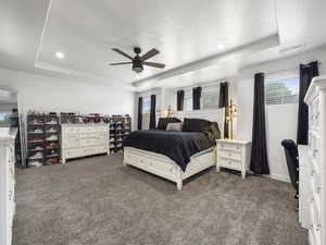 Bedroom with ceiling fan, dark colored carpet, a raised ceiling, and visible vents