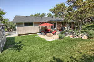 Back of property featuring an outdoor fire pit, a lawn, and a patio