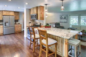 Kitchen featuring a kitchen breakfast bar, kitchen peninsula, pendant lighting, light stone counters, and stainless steel appliances