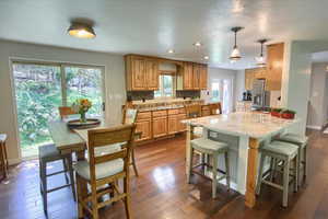 Kitchen with hanging light fixtures, decorative backsplash, stainless steel refrigerator with ice dispenser, sink, and dark hardwood / wood-style floors