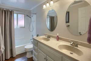 Full bathroom featuring vanity, shower / tub combo, toilet, ornamental molding, and hardwood / wood-style flooring