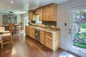 Kitchen featuring light stone countertops, dark wood-type flooring, light brown cabinetry, sink, and stainless steel dishwasher