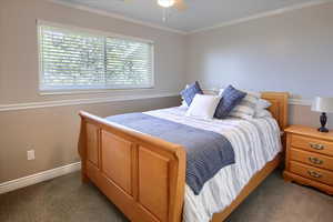 Bedroom with ceiling fan, dark carpet, and crown molding