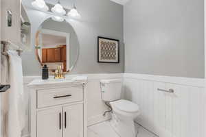 Half bathroom featuring marble finish floor, wainscoting, vanity, and toilet