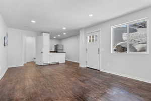 Unfurnished living room with a textured ceiling, dark wood-style flooring, recessed lighting, and baseboards