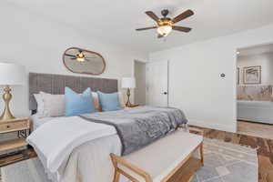 Bedroom with ceiling fan, ensuite bath, wood finished floors, and baseboards