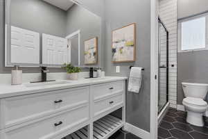 Bathroom featuring double vanity, a stall shower, toilet, tile patterned flooring, and a sink