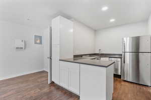 Kitchen with dark wood-style floors, dark countertops, appliances with stainless steel finishes, white cabinets, and a peninsula